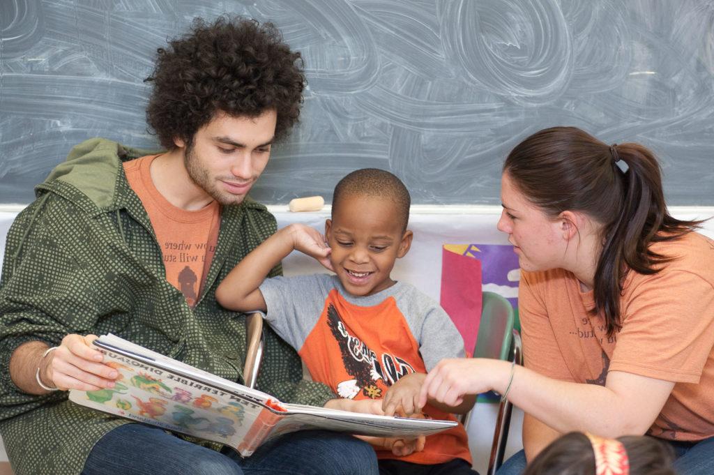 两个澳门威尼斯人网上赌场的学生在儿童教室里给一个小孩读一本图画书