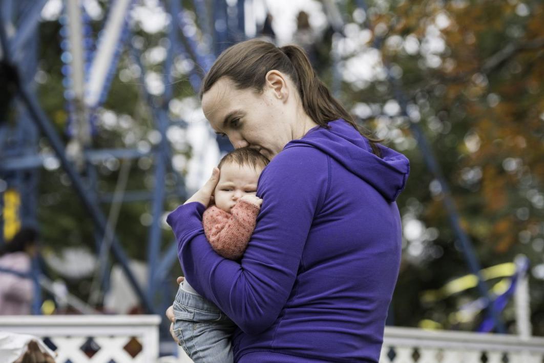 在罗彻斯特大学的梅利奥拉周末，一名年轻女子抱着婴儿站在摩天轮前